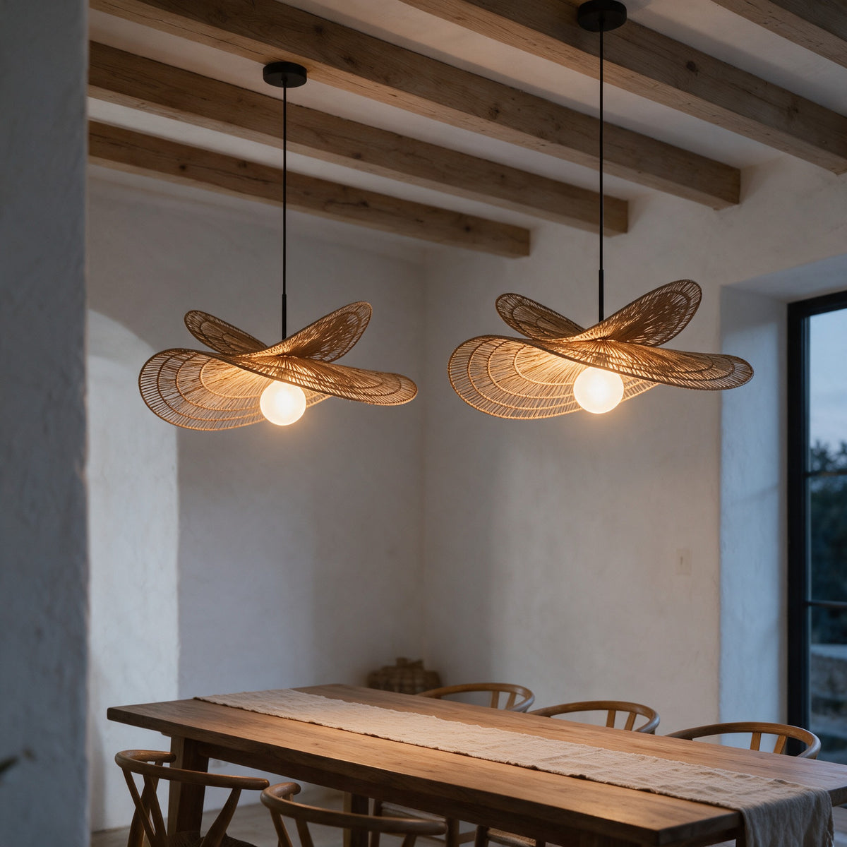 Two Isla rattan chandeliers hanging over a long oak dining table under wooden beams