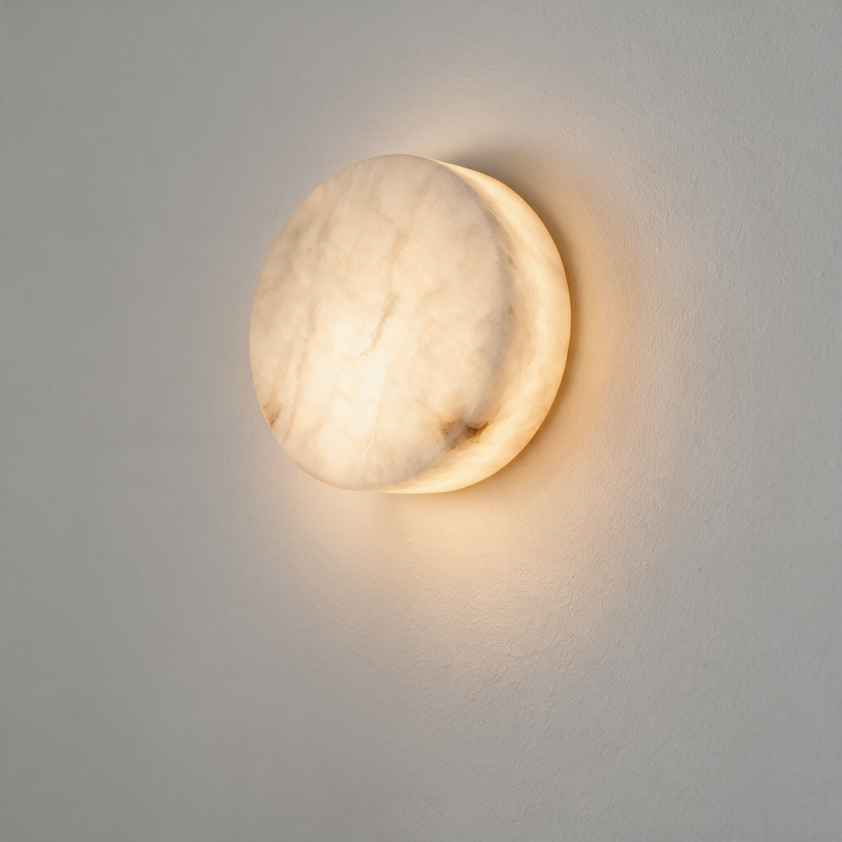 Davina Sconce – round alabaster wall light glowing warm on a white wall