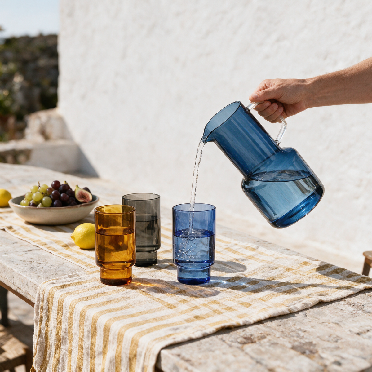 Palmarola cobalt carafe pouring water at a villa terrace lunch table with grapes and figs