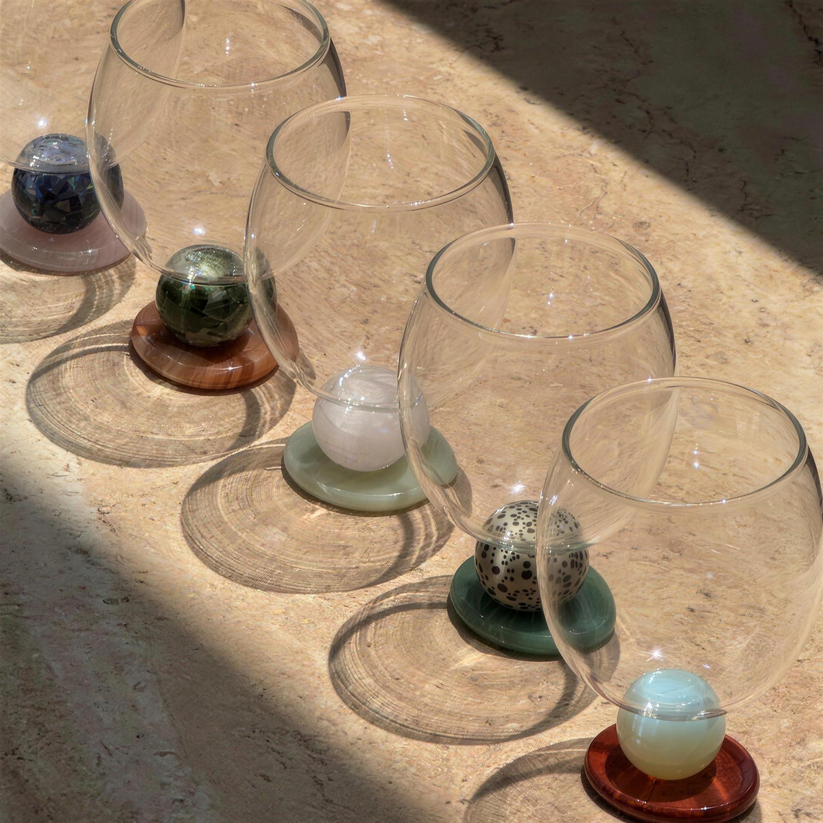 Row of Panarea goblets in different stone colours on sunlit travertine