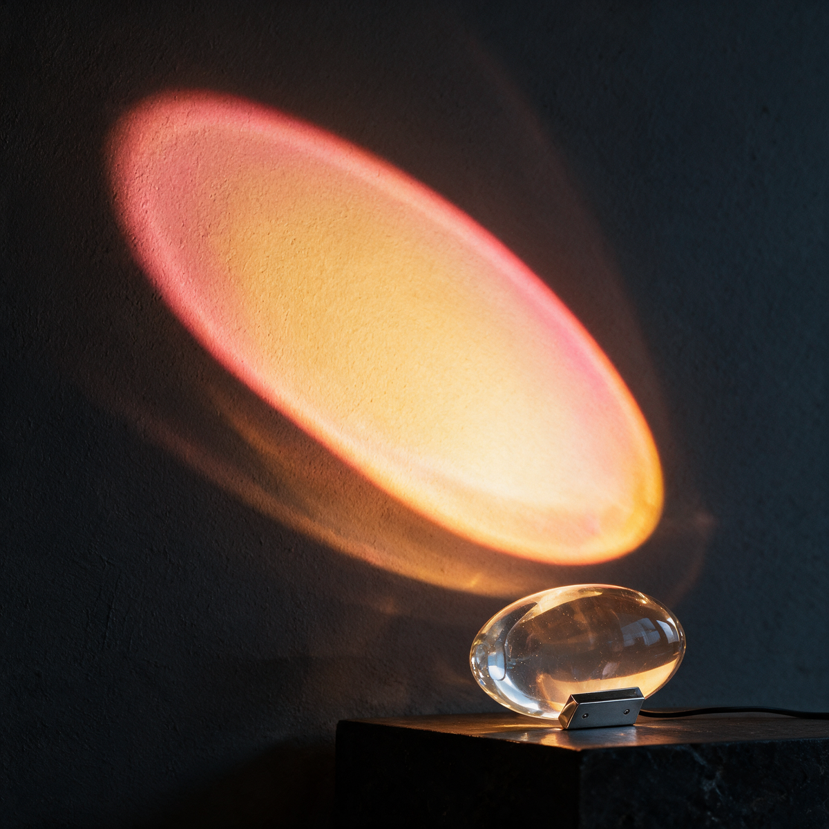 Sunlight Table Lamp casting a golden sunset glow on a dark wall from a black stone plinth