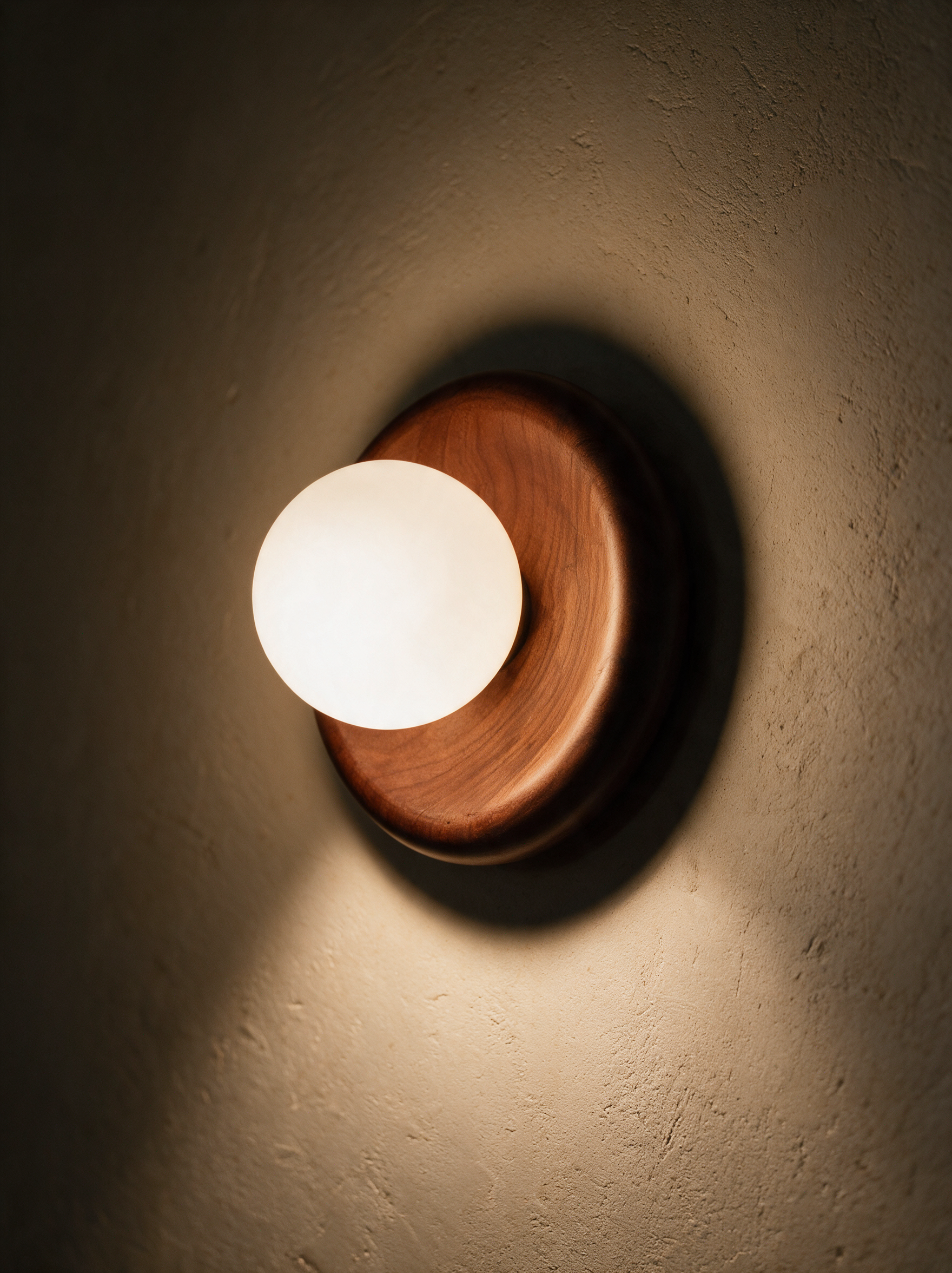 Marlow walnut wall sconce lit on a warm plaster wall, casting up and down glow