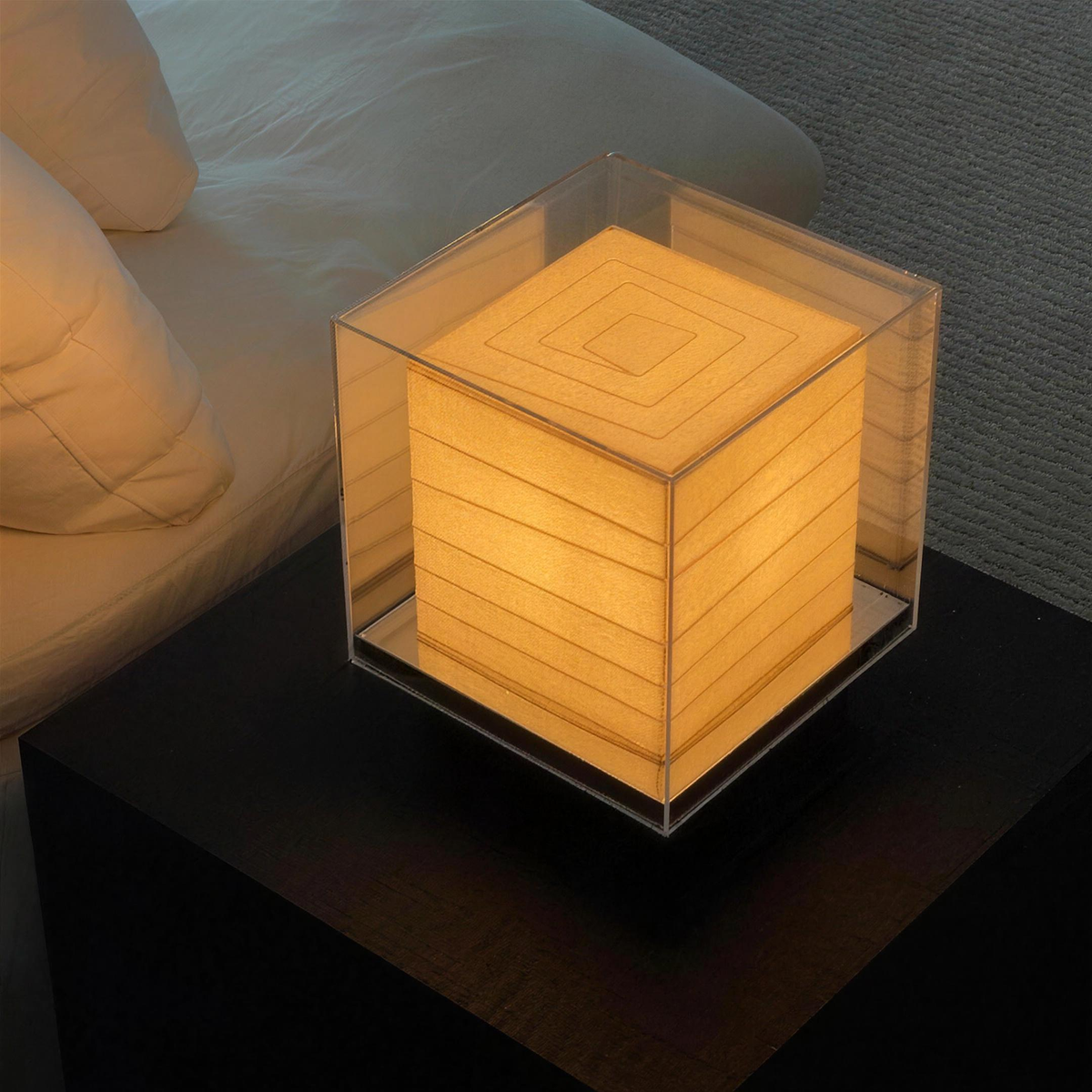 Kumo Table Lamp glowing on a dark bedside table beside the bed