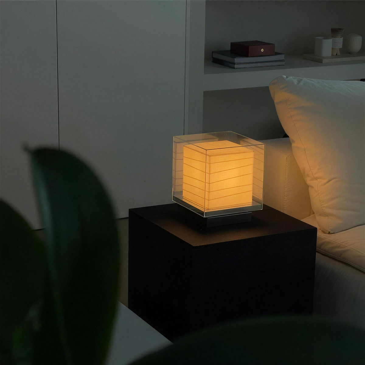 Kumo Table Lamp lit on a dark pedestal in a living room
