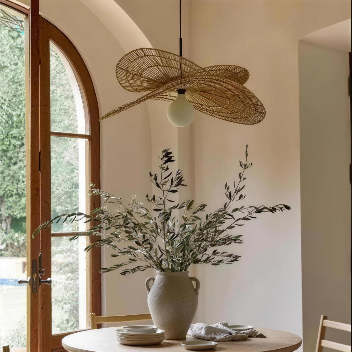 Isla rattan chandelier beside an arched window with an olive branch vase