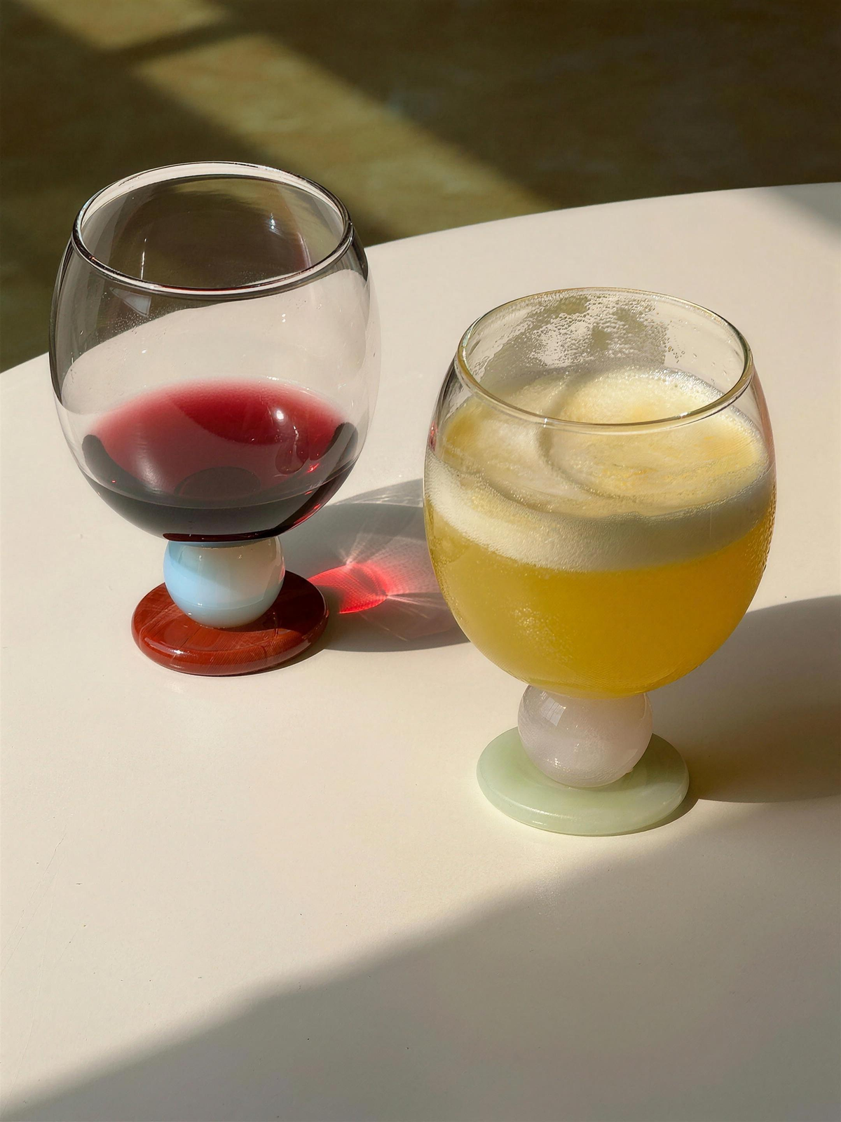 Red wine and fresh juice in Panarea goblets on a white table